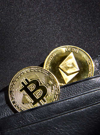 on a black background with a bokeh with sequins is a black leather wallet purse for money with a coin of currency crypto etheterium and bitcoinの写真素材