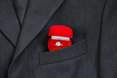 in the breast pocket of a dark black man's jacket in a light strip is a red box for the ring of the weddingの写真素材