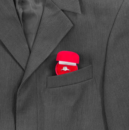 In the breast pocket of a dark black man's jacket in a light strip is a red box for the ring of the weddingの写真素材