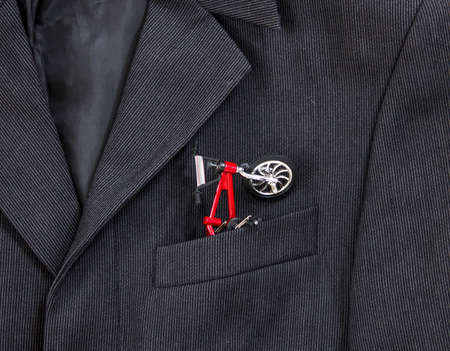 In a breast pocket of a dark black man's jacket in a light strip there is a bicycle with a red frameの写真素材