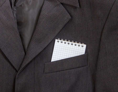 In a breast pocket of a dark black man's jacket in a light strip lay a notebook on springs in a cageの写真素材