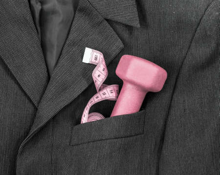 In a breast pocket of a dark black man's jacket in a light strip lies sports equipment tape centimeter pink dumbbellの写真素材
