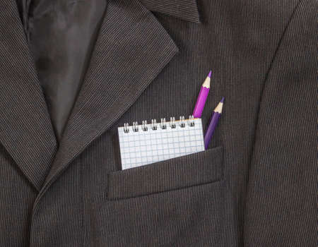In the breast pocket of a dark black man's jacket a bright strip of pencils of purple and lilac color and notebook on the springs in the cageの写真素材
