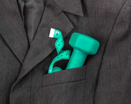 In a breast pocket of a dark black man's jacket in a light strip lies sports equipment tape centimeter green dumbbellの写真素材