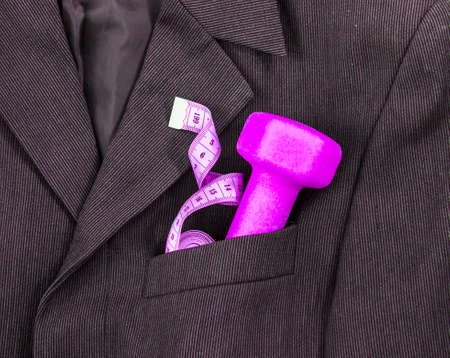 In a breast pocket of a dark black man's jacket in a light strip lies sports equipment tape centimeter purple dumbbellの写真素材