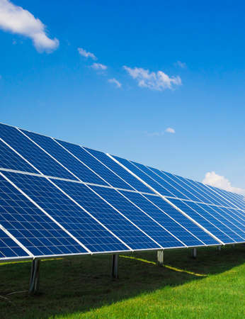 Solar panels of a battery of photocells against a background of clouds and a blue sky green grassの写真素材