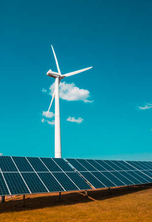 wind generator of electricity from three blades and solar panels of a battery of photocells against a background of clouds and a blue sky orange grassの写真素材