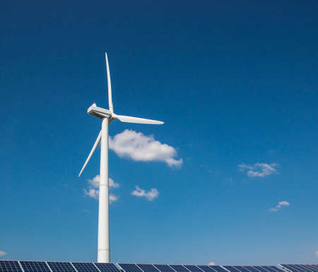 wind generator of electricity from three blades and solar panels of a battery of photocells against a background of clouds and a blue sky green grassの写真素材