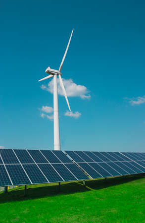 wind generator of electricity from three blades and solar panels of a battery of photocells against a background of clouds and a blue sky green grassの写真素材