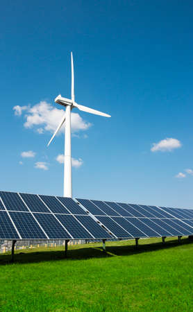 wind generator of electricity from three blades and solar panels of a battery of photocells against a background of clouds and a blue sky green grassの写真素材