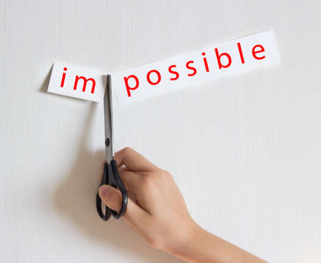 on a light background a hand holds a pair of scissors cuts a piece of paper an inscription red color is impossibleの写真素材