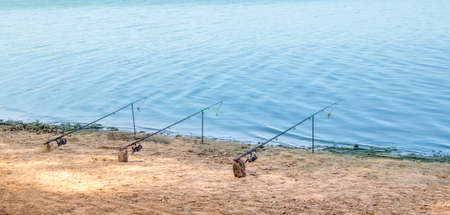 near the blue sea water river stand three fishing rods on the yellow sand fishingの写真素材
