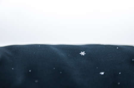 on a dark green cloth, snow and one clear snowflake on a white backgroundの写真素材
