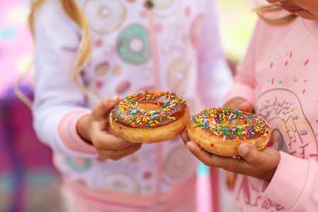two girls are holding a sweet and a big donut decorated with pink icing and confectionary dressingの写真素材