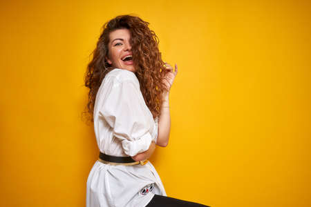 Portrait of a young beautiful girl with curly hair. She's wearing a white shirt. Cheerful, joyful, happy. It is photographed on a solid yellow background.の写真素材