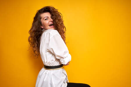 Portrait of a young beautiful girl with curly hair in a white shirt on a bright yellow monochrome background. A real person who enjoys life.の写真素材