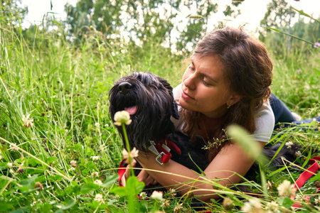 a young pretty girl in a white T-shirt lies on the grass in nature with a black Mittelschnauzer dog and hugs. Space for text. leisure, people, adorable domestic pets concept. love and care for animalsの写真素材