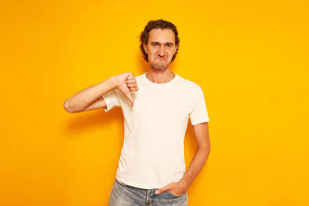 man in casual clothes with a dissatisfied face shows a thumb at bottom as a sign of poor quality denial. insulated on yellow background with space for text. concept of people, service, evaluationの写真素材