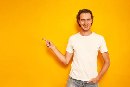 a happy smiling curly-haired man in casual clothes points his finger at the empty space for ad text. isolated on a yellow background. concept of people promotions, discounts, advertising offer, indexの写真素材