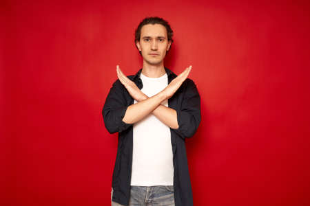 serious negative man unhappy sad crossed hands show no stop decline reject sign isolated over red color background with free space for text. concept protest, disagreement, blocking, timeout, game overの写真素材