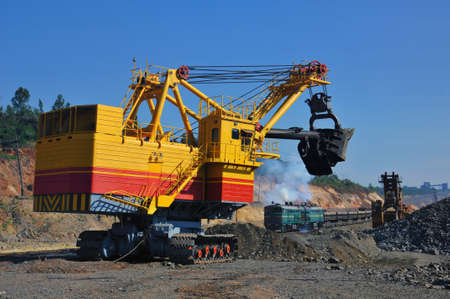 Excavator loading iron ore into goods wagon on the iron ore opencast mine