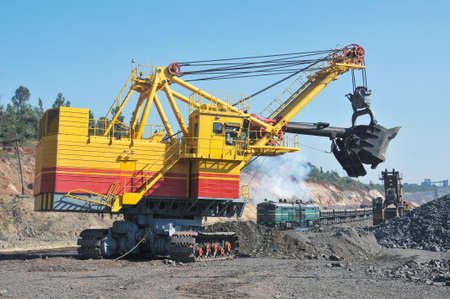 excavator loading iron ore into goods wagons in opencast mine
