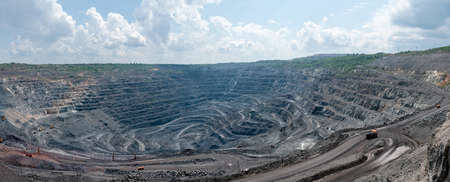 panorama of quarry extracting iron ore with heavy trucks, excavators, diggers and locomotives