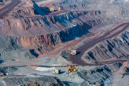 close up of open cast mine extracting iron ore with heavy trucks, excavators, diggers and...