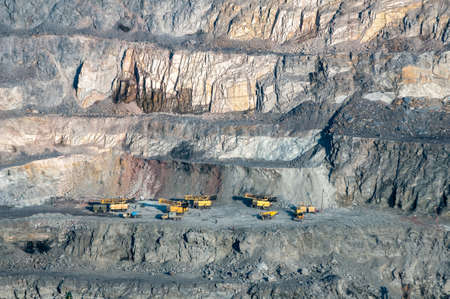 close up of open cast mine extracting iron ore with heavy trucks, excavators, diggers and...