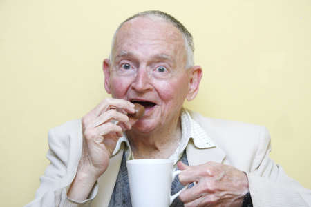 elderly man drinking coffee and eating chocolateの写真素材