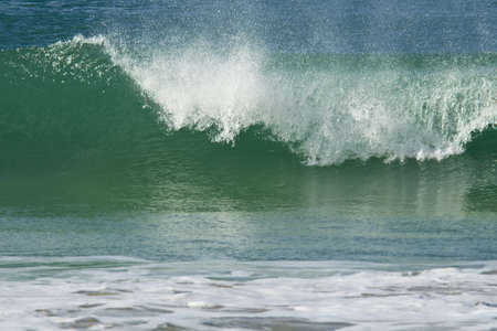 beautiful wave breaking with the crest of white water being blown by the wind