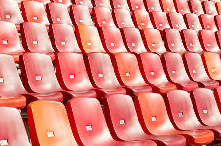 straight rows of red chairs in a sports stadium photographed at an angleの写真素材