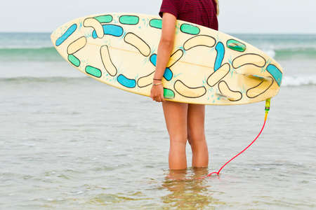 Surfer standing in shallow water looking for waves hold her board