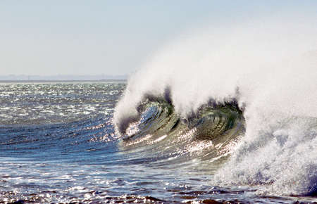strong wing blowing causing sea spray on a large breaking wave