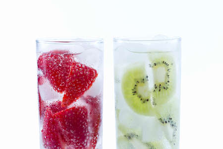 Two ready to drink glasses filled with strawberries and kiwis filled with ice on a white backgroundの写真素材