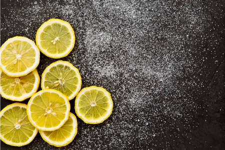 sliced lemons with sprinkled sugar on a dark grey background
