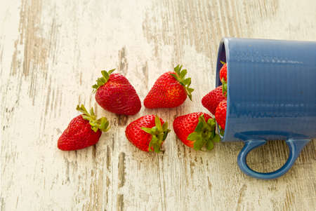 Blue mug pouring out red ripe strawberries onto a white wooden backgroundの写真素材