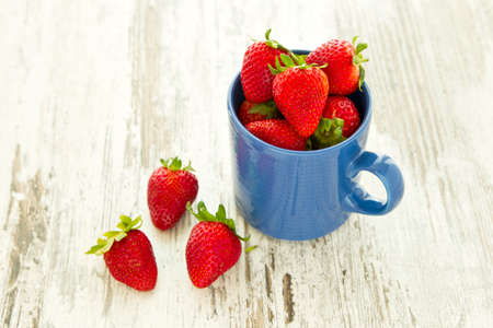 Blue mug filled to the brim with beautiful ripe red strawberries on a white wooden backgroundの写真素材