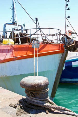 Old fishing boat tied to the harbor quay side with ropeの写真素材