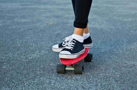 Two feet of a young woman standing on a red skate board while on a asphalt roadの写真素材