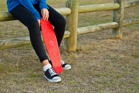 Young woman sitting on a wooden fence with her skate board between her legs 