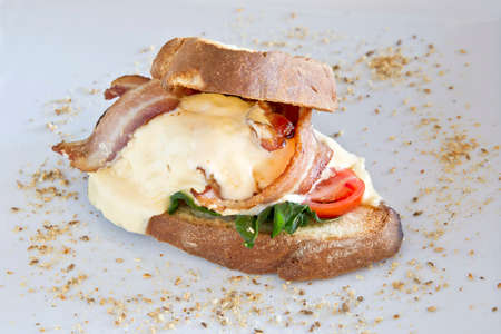 large tasty bacon and poach egg wrapped in ciabatta bread on a white plateの写真素材