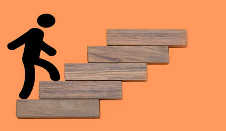 person climbing wooden stairs to the top concept on a orange backgroundの写真素材