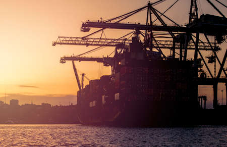 Sillhoette of a large container vessel in port being offloaded by huge cranes at sunsetのeditorial素材