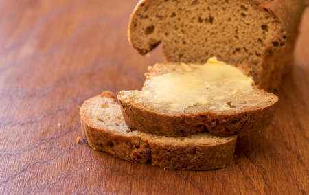 Slices of banana bread with fresh butter on a wooden cutting board with copy space on the left