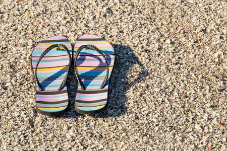 Pair of beach sandals with stripes lying on a stony beach beach early on a sunny morning の写真素材
