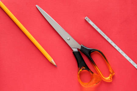 Items of stationery placed on a red background taken from above scissors,pencil,measuring tapeの写真素材