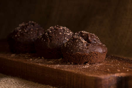 Tasty fresh chocolate muffins on a wooden platter in soft window light photographed in a darkfood...
