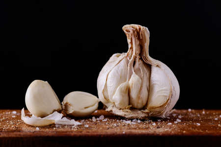 Garlic cloves with added spices broken up and ready to be used on a wooden board and black backgroundの写真素材