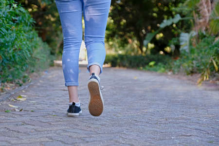 young woman with blue jeans walking away from camera on a paved pathway in a tropical forestの写真素材
